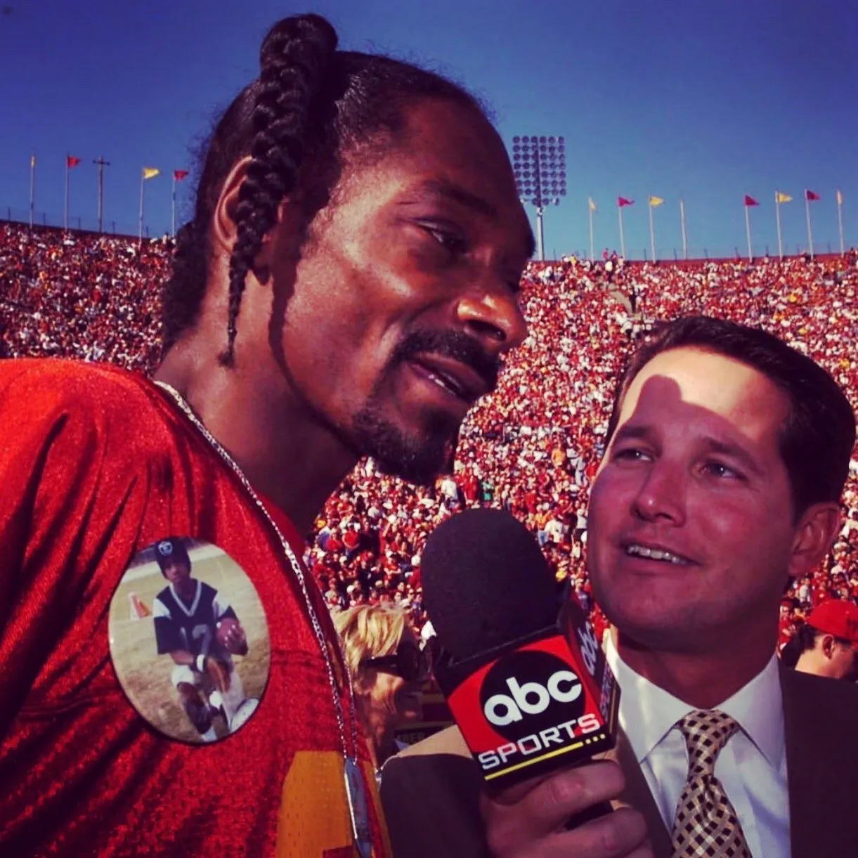 Todd Harris holding an ABC Sports microphone beside Snoop Dogg in a packed stadium.