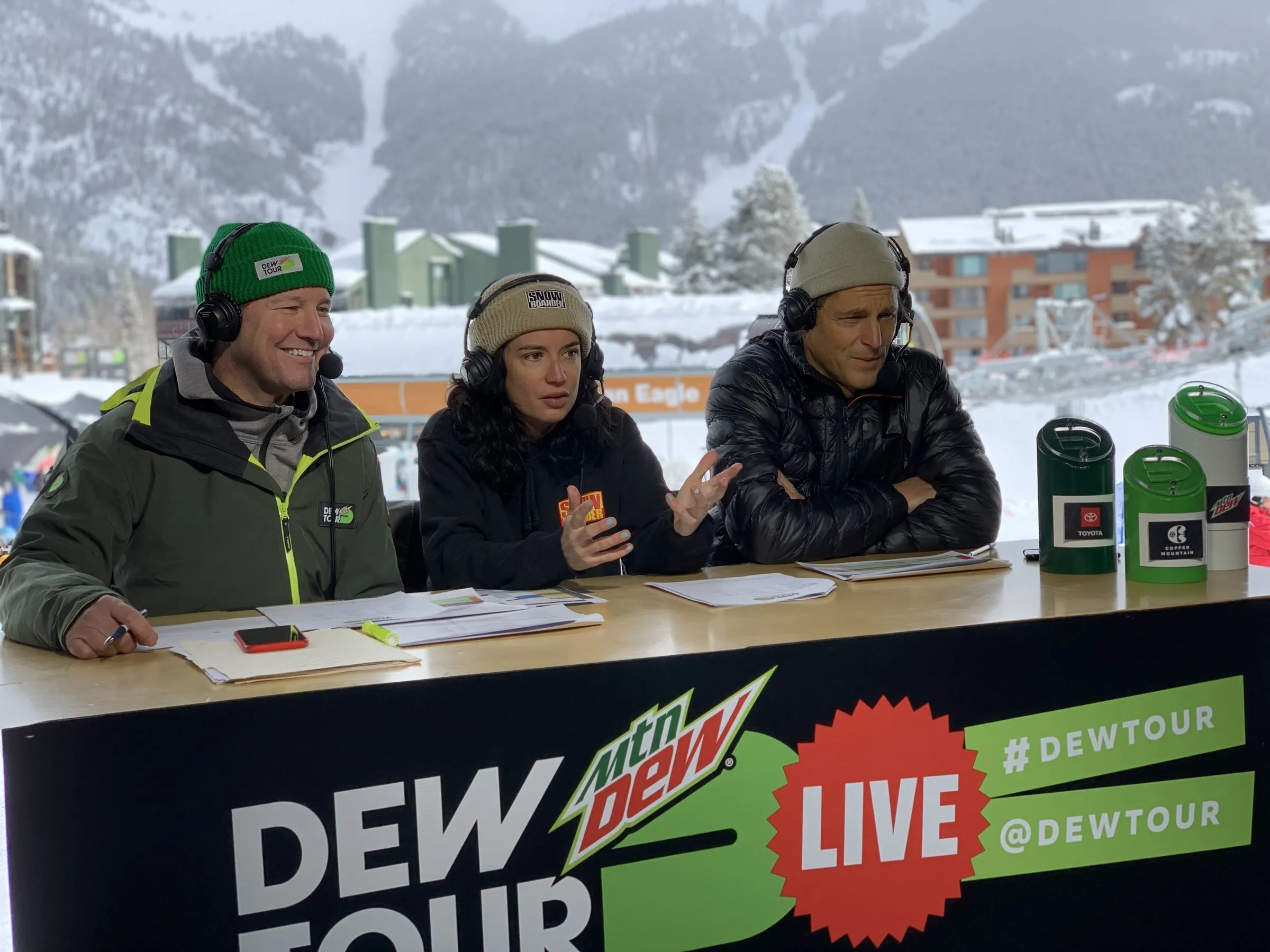 Todd Harris hosting the Dew Tour Live desk in snow, flanked by two co-hosts.