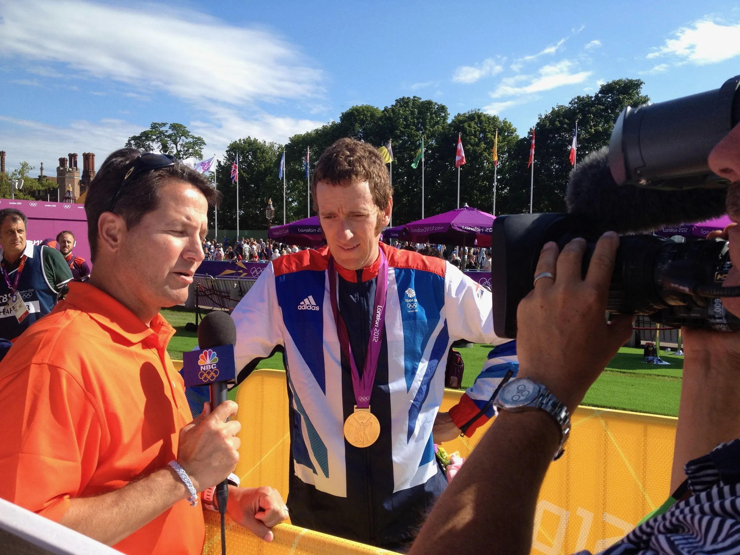 Todd Harris interviewing a gold medallist on camera, the medal held up between them.