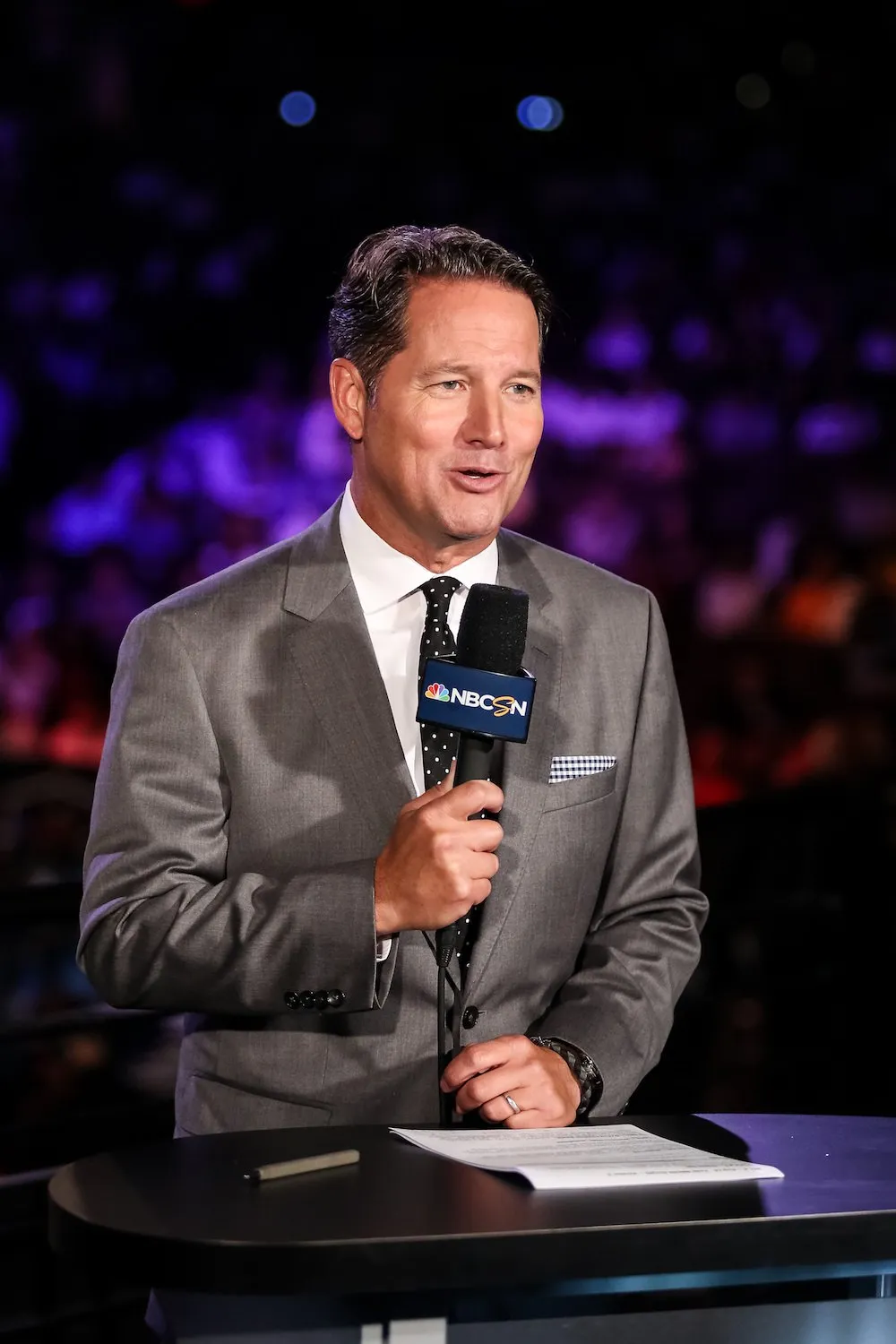 Todd Harris on the PFL desk with a handheld microphone under arena lighting.