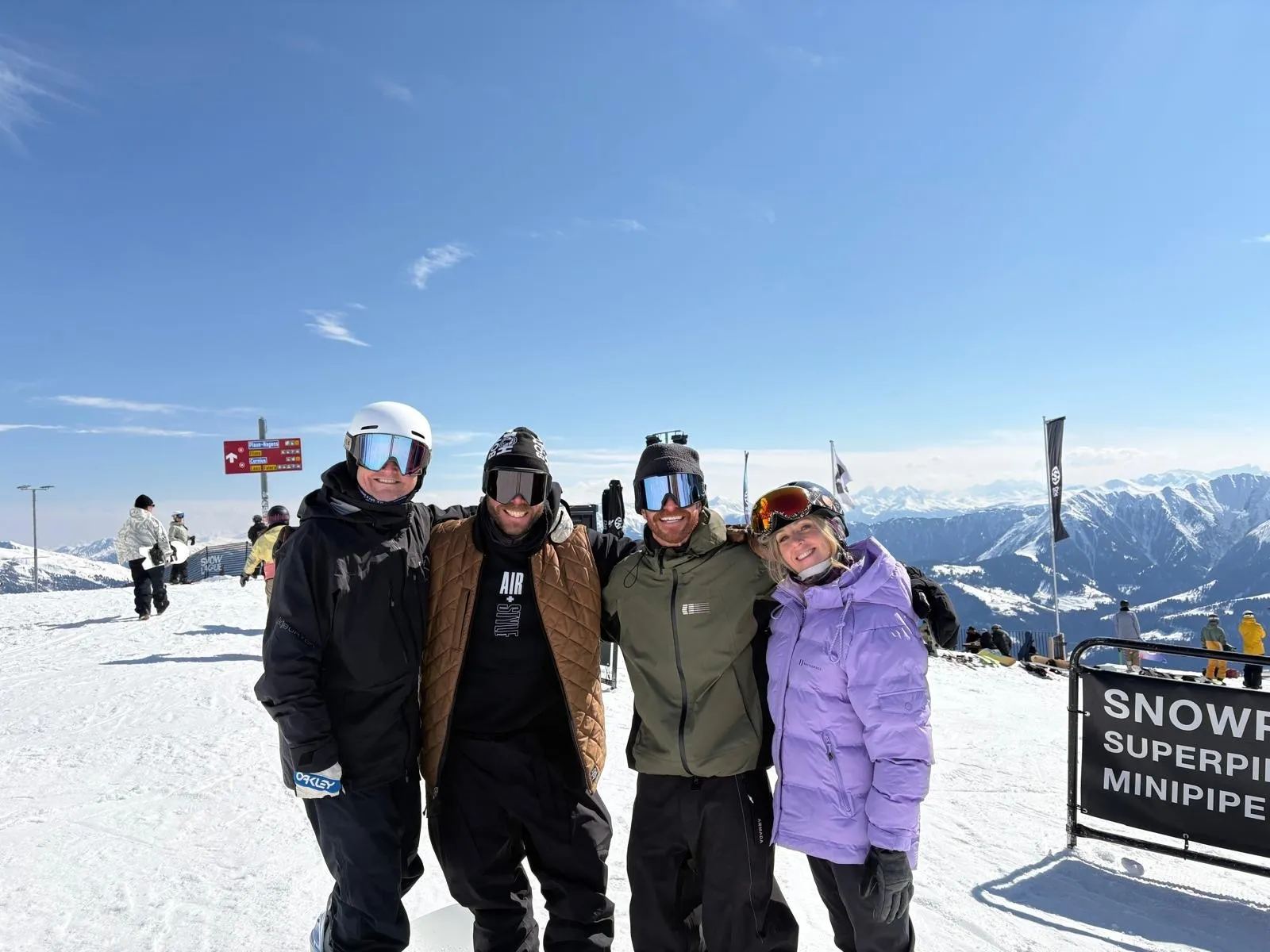 Todd Harris and the Snow League crew in goggles at the top of the superpipe, mountains behind them.